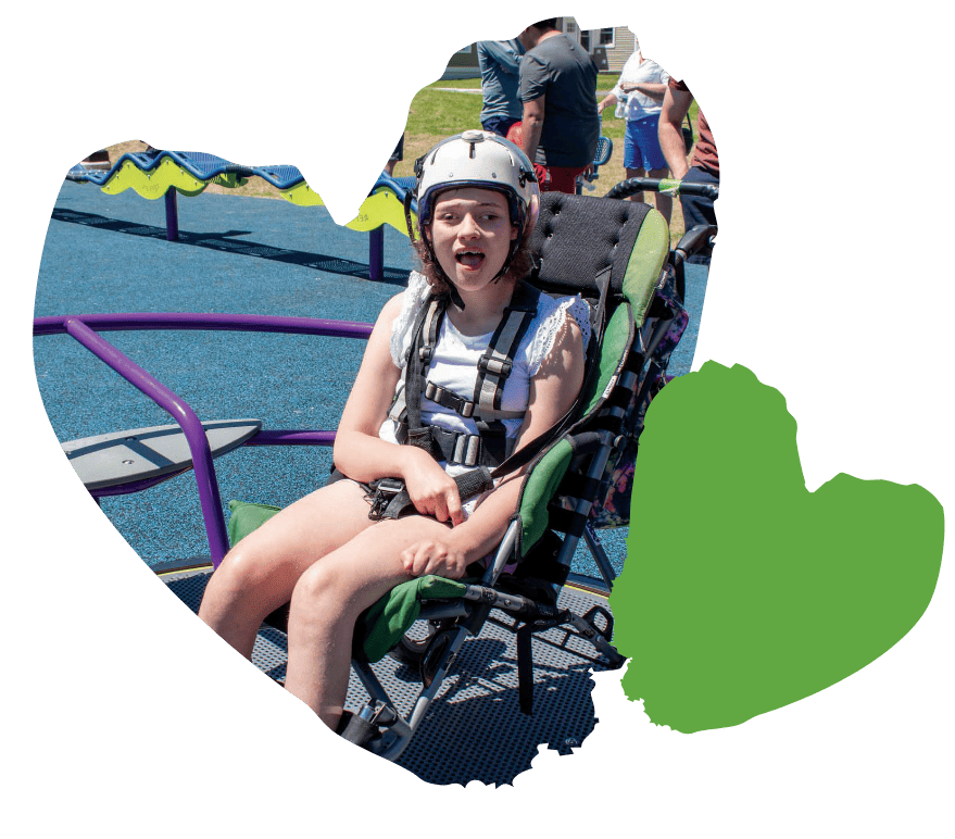 Amidst a colorful backdrop, a person in a wheelchair, wearing a helmet, joyfully explores an adaptive playground designed for everyone to enjoy outdoor activities.