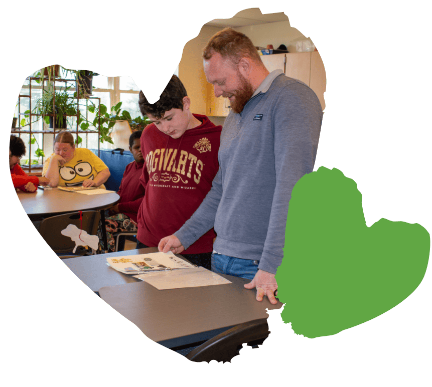 student and adult flipping though book on desk in classroom