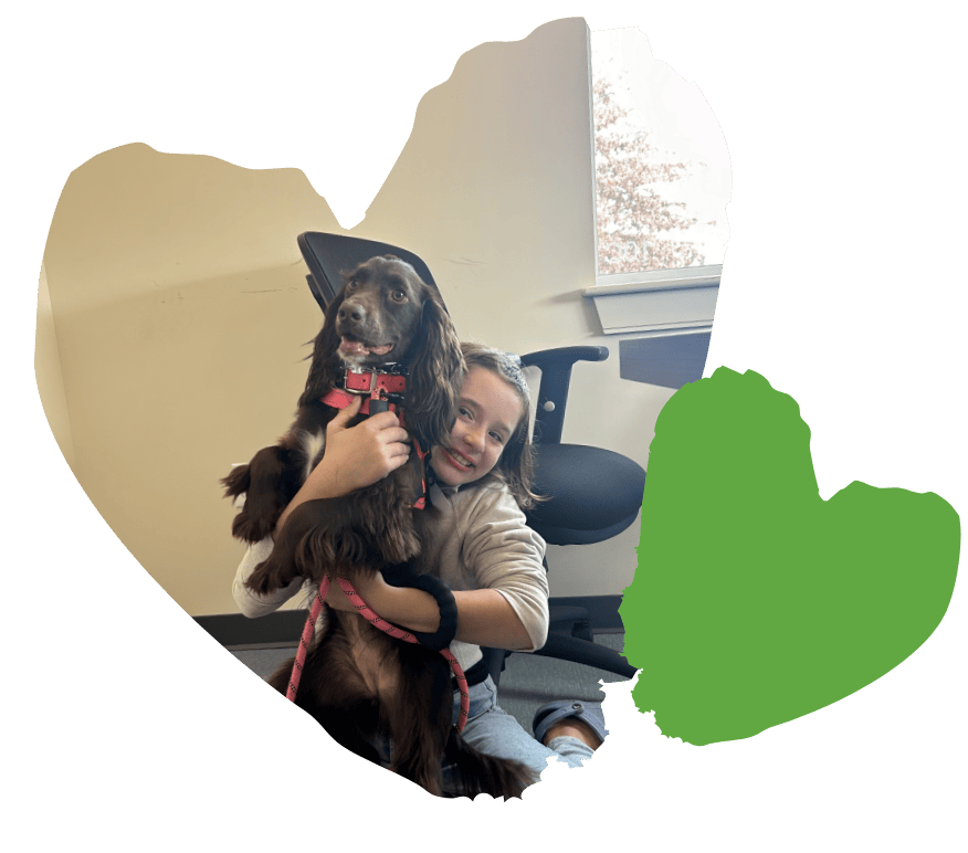 In an office setting, a child gleefully hugs a brown dog, embodying the warmth and support often found in behavioral services.
