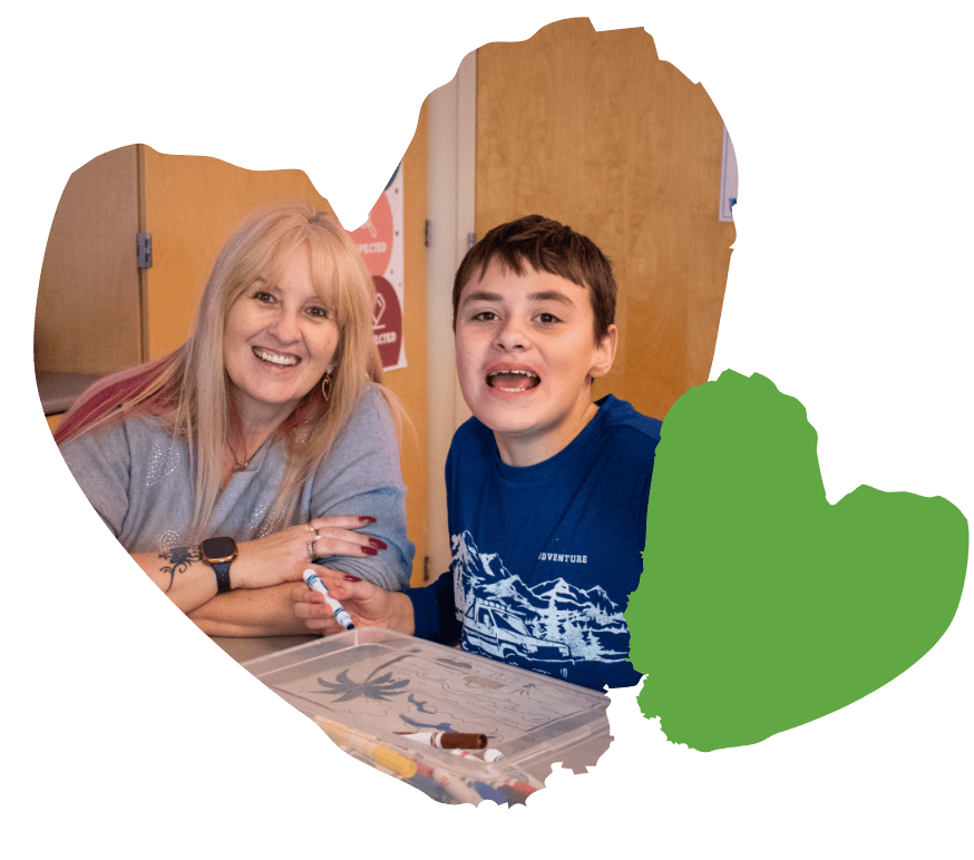 Woman and boy smiling while doing arts and crafts at a table.