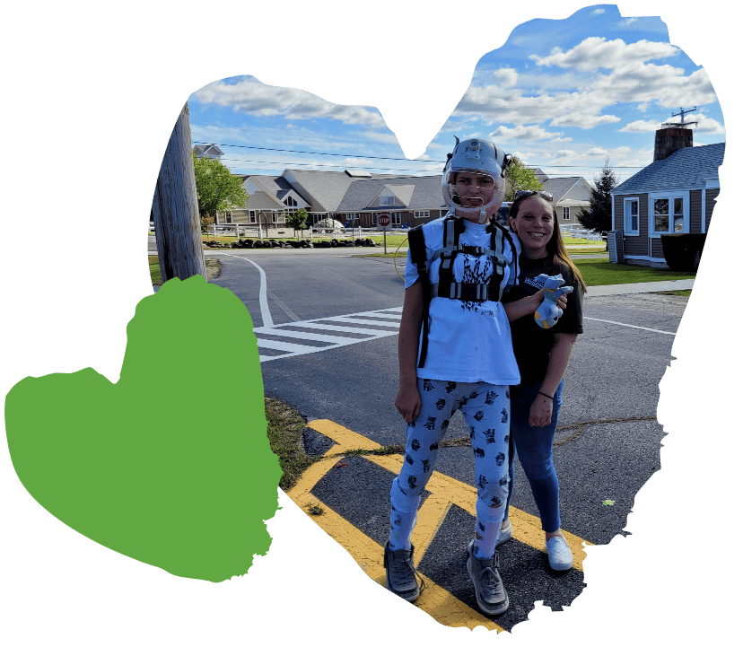 Two people stand on a street, smiling. One wears braces; the sky is partly cloudy. A green heart decorates the image.