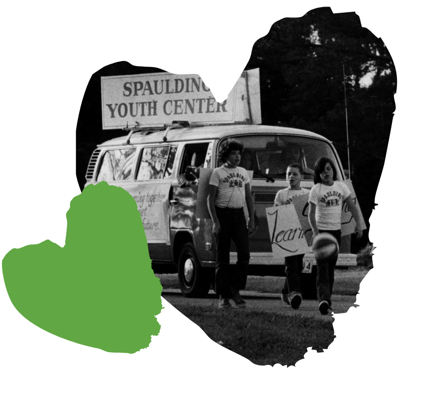 Three people walking in parade with a Spaulding Youth Center sign, carrying a ball.