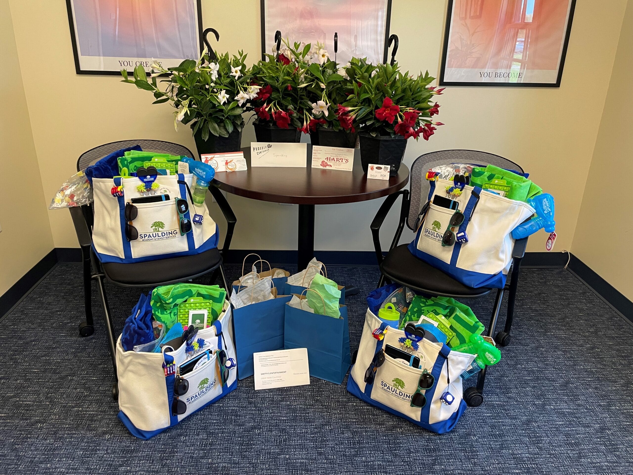 Four gift bags filled with beach toys and essentials on chairs around a table with plants and cards.