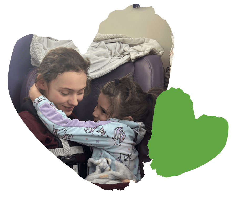 A young woman and a little girl hug and smile at each other, sitting closely on a seat with blankets.