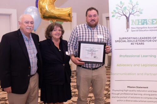 Three people posing with an award certificate beside a NHASEA banner and a gold balloon shaped as the number two. Three people posing with an award certificate beside a NHASEA banner and a gold balloon shaped as the number two.